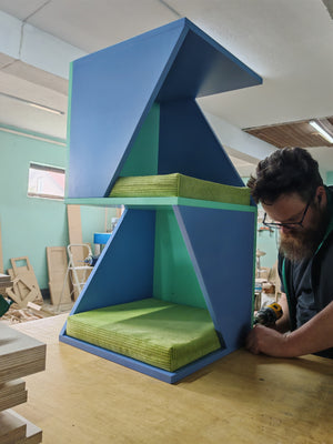 the picture shows finishing assembly of a multilevel cat tower. It combines haven blue with a mint middle and backdrop plates. The cushions are stripped velvet in light but vibrant green. The shelf is fun, modern and unique.