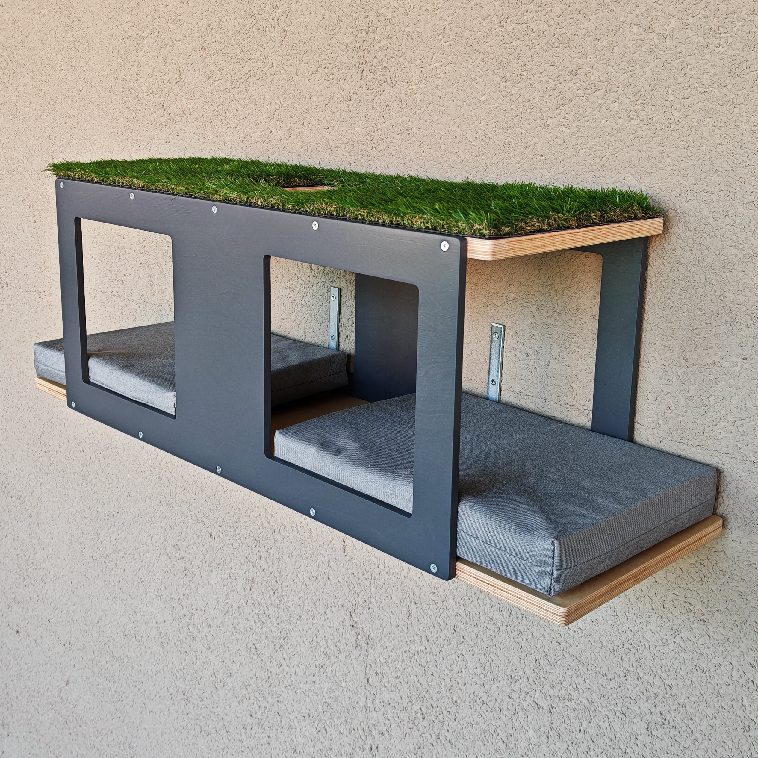 Catio shelf for large cats. Made for mounting on steel mesh or on wooden or metal beams. It has multiple entry points and 4 large windows. The fronts and back(accents) are in dark grey, and the base wood is in natural birch. There are two large grey cushions on the bottom larger shelf. The top has an opening in the middle and is carpeted with artificial grass. It comes fully assembled and ready for installation. Mounting hardware is included. 