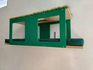 Outdoor enclosure mesh mounted big cat shelf. It's a multilevel platform with multiple entry points and windows. There are 2 comfortable cushions on the lower level. The top level is carpeted with artificial grass. The base color is natural, while the accent is emerald green. The cushions are in tenda green. 
